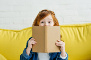 Young girl holding a book on a yellow sofa