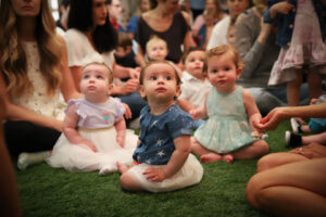 Group of toddlers sitting on an astroturf carpet looking up at a teacher reading to them