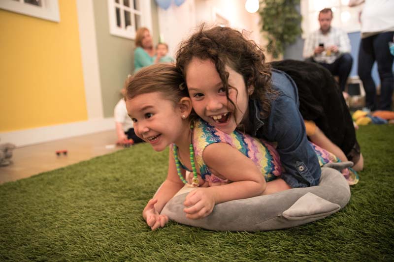 two female students horsing around wrestling on an astroturf rug