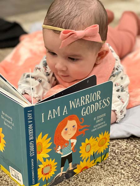 Toddler with a bow on her head reading a book