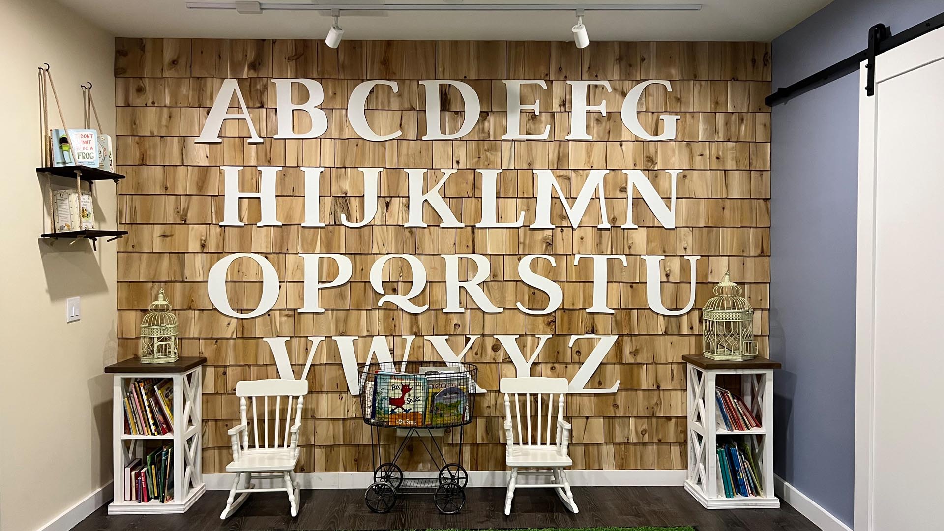 Wall of white letters on cedar shingles with child-sized furniture in front of it at Wise Wonder West End