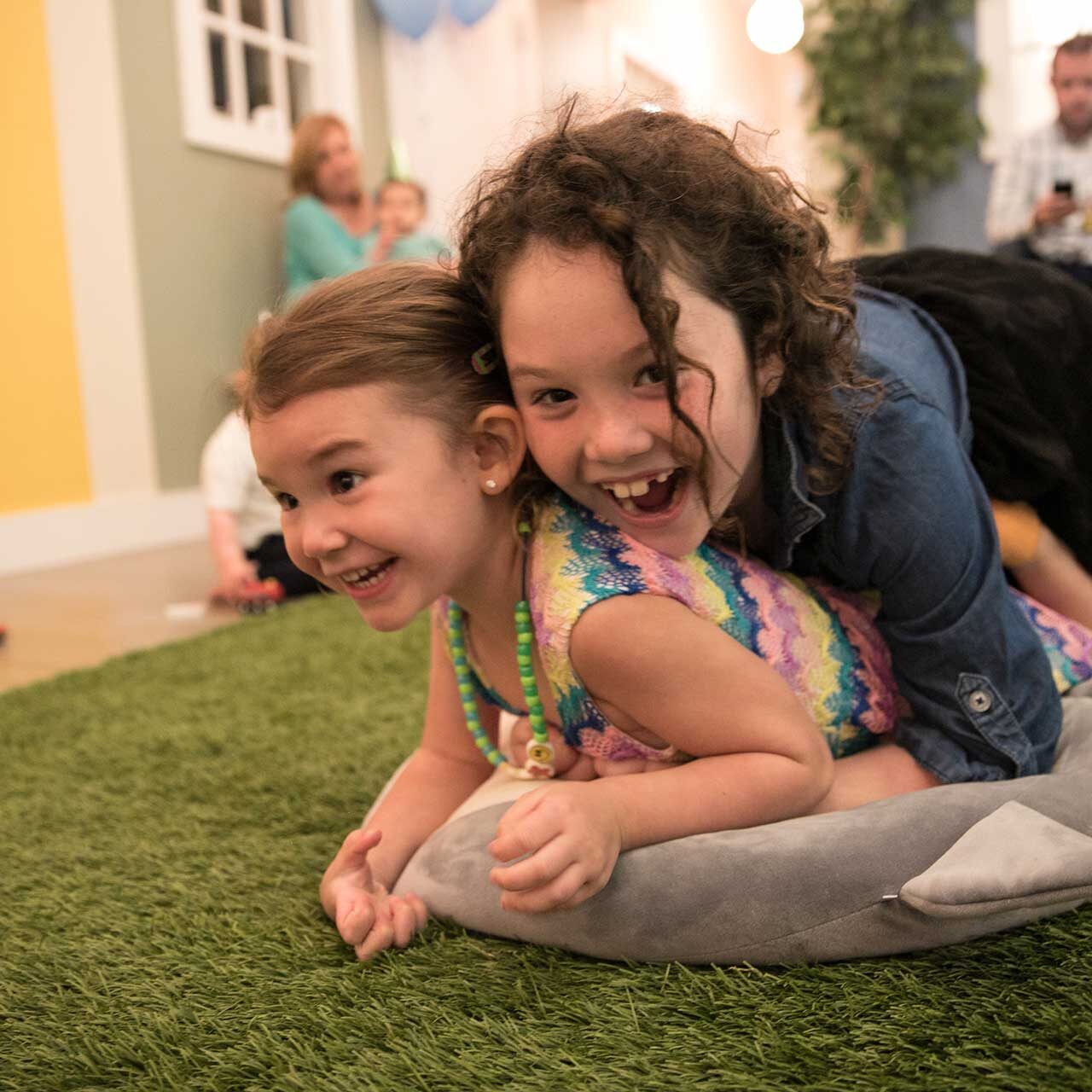 Two girls wrestling on the astroturf floor of Wise Wonder Enrichment